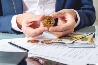 Bir madeni para bitcoin tutan belgelerle masada oturan işadamı bankacı. Exchange ve cryptocurrency Euro için satışı kavramı
