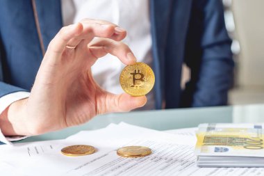 Bir madeni para bitcoin tutan belgelerle masada oturan işadamı bankacı. Exchange ve cryptocurrency Euro için satışı kavramı