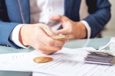 Bir madeni para bitcoin tutan belgelerle masada oturan işadamı bankacı. Exchange ve cryptocurrency dolar satışı kavramı