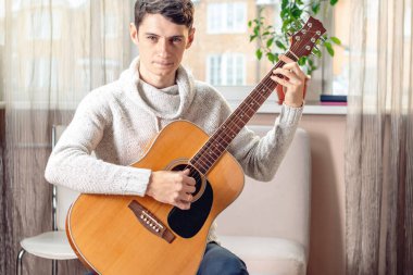 Akustik gitar çalmak bir sandalyede oturan genç çekici erkek müzisyen. Bir hobi olarak müzik kavramı