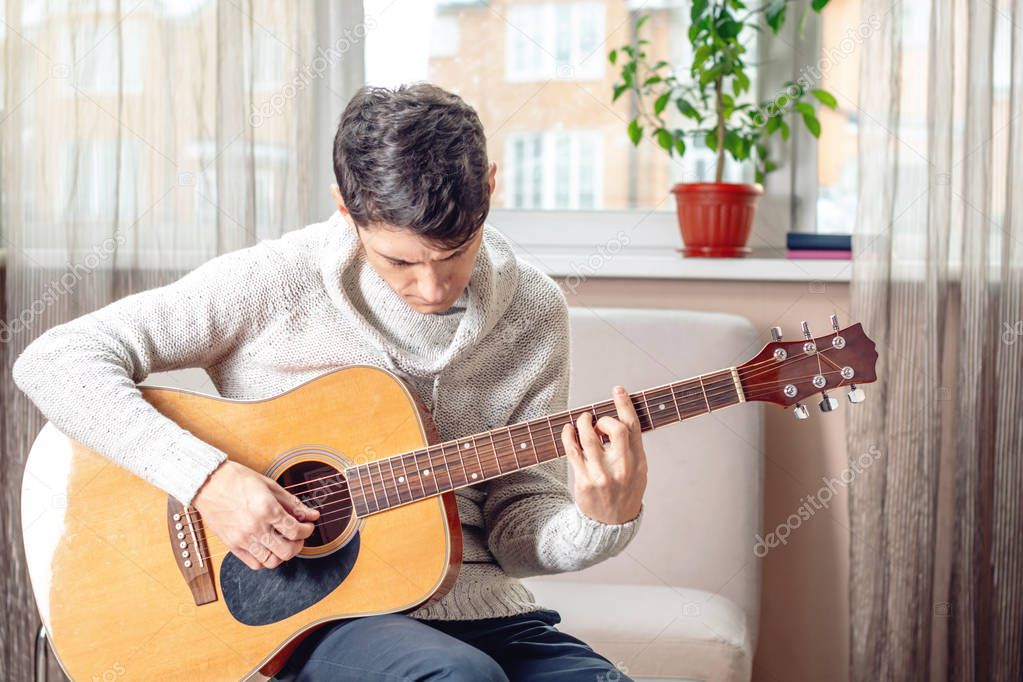 Young attractive male musician sitting on a chair playing acoustic guitar. The concept of music as a hobby
