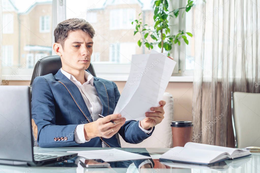 Male Manager sitting at a work place examing documents. The concept of the office working with documents