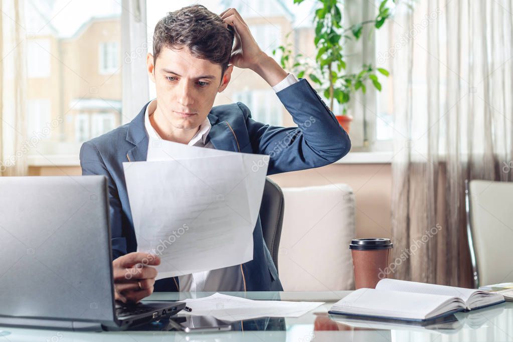 Male businessman sitting at a work place examing documents. The concept of the office working with documents