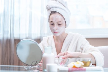 Mutlu genç kadın güzel yüzünde cilt nemlendirici krem doğal kozmetik uygulama başında bir havlu ile. Hijyen ve bakım cilt evde kavramının