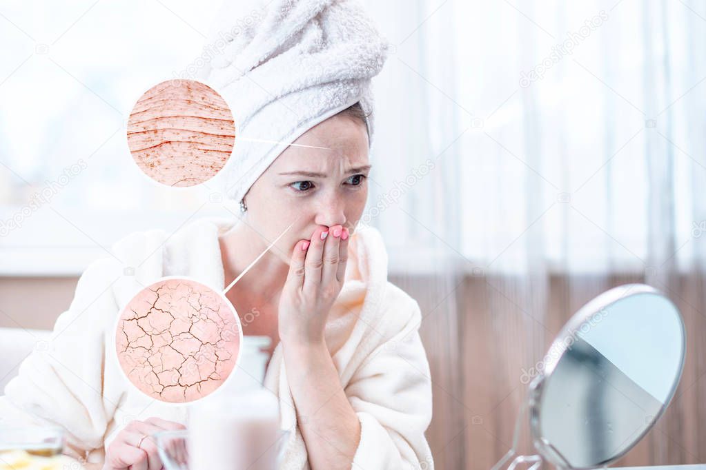 Beautiful young woman with a towel on her head looking at her dry skin with cracks and with first wrinkles. Circles increase the skin like a magnifying magnifier