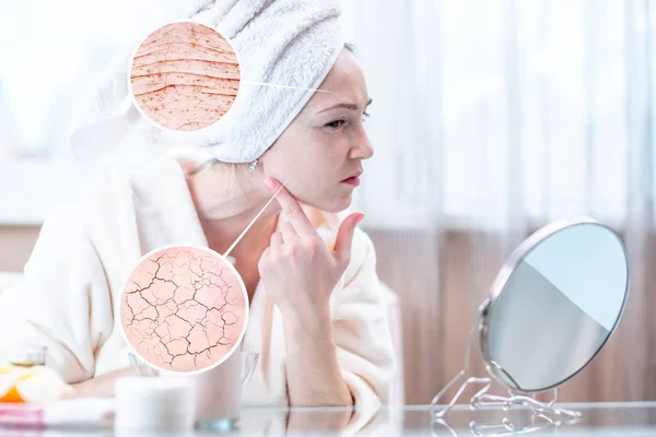 Beautiful young woman with a towel on her head looking at her dry skin with cracks and with first wrinkles. Circles increase the skin like a magnifying magnifier