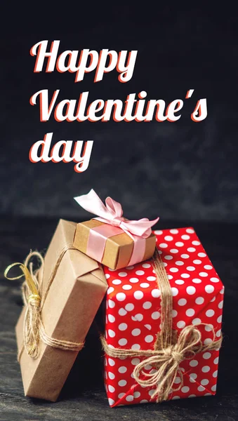 Holiday gift boxes Packed in crafting paper and red polka dots on dark wooden background. Vertical card Happy Valentine\'s day with text