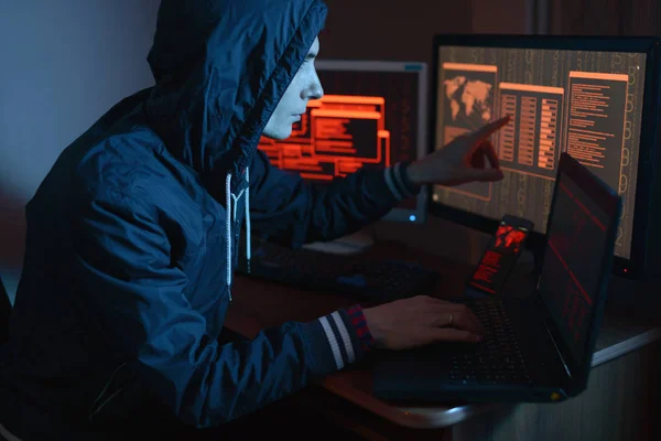 引擎盖中的男性黑客将手指指向显示网络攻击和黑暗中屏幕背景上的黑客攻击数据的显示屏 网络安全的概念 — 图库照片