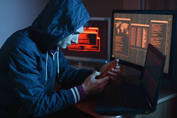 男子黑客在引擎盖里拿着手机在他的手中试图黑客移动设备云 并窃取数据在霓虹灯 网络安全的概念 — 图库照片