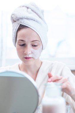 Mutlu genç kadın güzel yüzünde cilt nemlendirici krem doğal kozmetik uygulama başında bir havlu ile. Hijyen ve bakım cilt evde kavramının