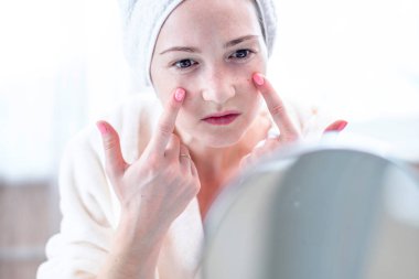 Kafasındaki bir havlu ile genç kadın güzel yüzünde sivilce algılar. Hijyen ve cilt için bakım kavramı