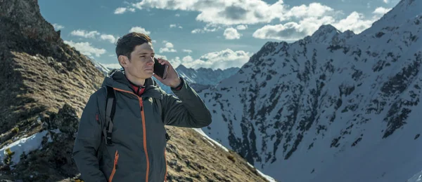 A young man with phone in hand on the top of a snowy mountain far from civilization on a background of blue sky. The concept of activity and the availability of mobile connection