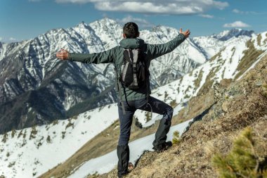 Erkekler Turizm güneşli bir günde karlı dağlar arka plan üzerinde duran kolları yayarak başarısını kutlamak. Motivasyon ve hedeflerine ulaşılmasına kavramı