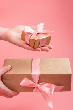 Kraft kağıt pembe bir arka plan üzerinde hediye kutusunda paketlenmiştir holding eller. Sevgililer günü ve kadınlar günü kavramı tatil kartı