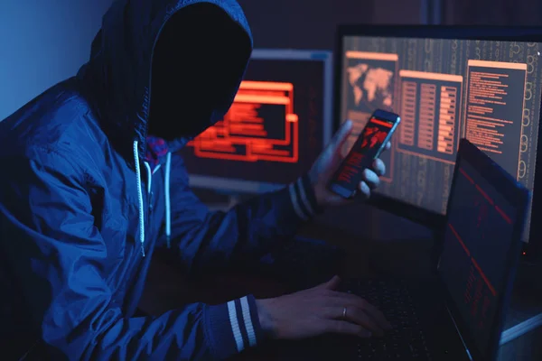 An anonymous hacker with no face typing the code tries to hack the system and steal accesses on the background screens in neon light. The concept of cybersecurity