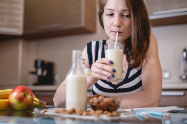 Mutfakta elinde bir bardak tutan organik badem sütü içen kadın. Şişe ve meyve masada. Sağlıklı vejetaryen ürün