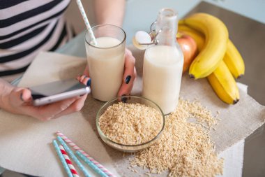 Mutfakta elinde bir bardak tutan organik pirinç sütü içen kız. Şişe ve meyve masada. Yukarıdan manzara. Diyet sağlıklı vejetaryen ürün