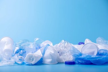 Bir yığın içinde temiz plastik çöp kullanılır. Mavi arka planda şişeler ve çantalar. Atık sıralama kavramı