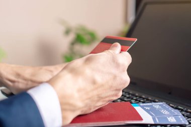 Elinde banka kartı tutan adam dizüstü bilgisayar kullanarak internet uçak biletlerini satın alıyor. Online satın alma ve rezervasyon konsepti