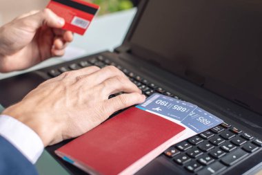 Elinde banka kartı tutan adam dizüstü bilgisayar kullanarak internet uçak biletlerini satın alıyor. Online satın alma ve rezervasyon konsepti
