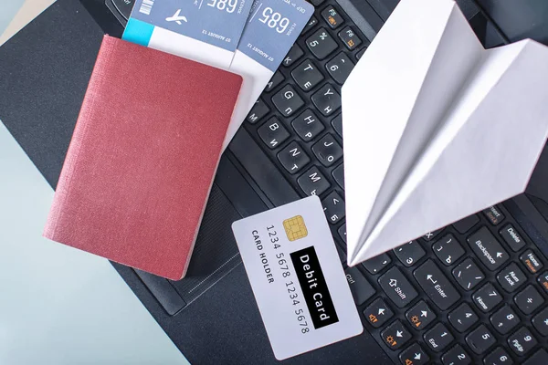 Airline tickets, passport, debit card and paper plane are on the laptop keyboard. The concept of purchasing and booking online