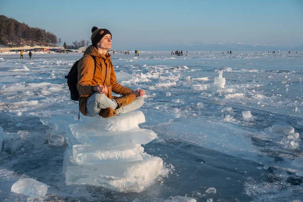 Man toerist met een rugzak mediteert zittend in de lotuspositie op het ijs van het Baikalmeer — Stockfoto