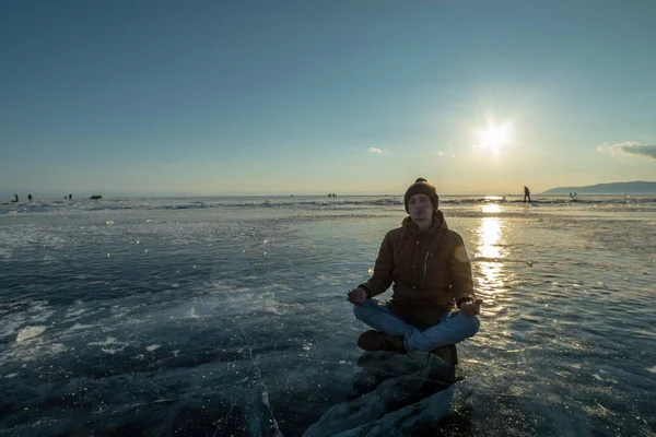 Турист с рюкзаком медитирует, сидя в позе Лотоса на льду озера Байкал. Спокойствие и свобода природы — стоковое фото