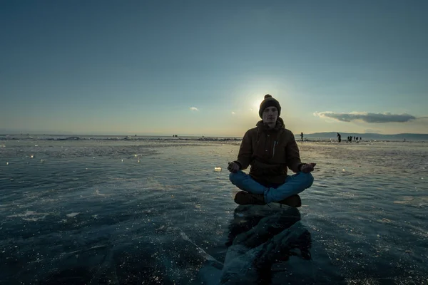Turista con una mochila medita sentado en posición de loto en el hielo del lago Baikal. Relajación y libertad de la naturaleza — Foto de Stock