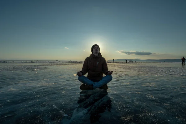 Tourist with a backpack meditates sitting in Lotus position on the ice of lake Baikal. Calm and freedom of nature
