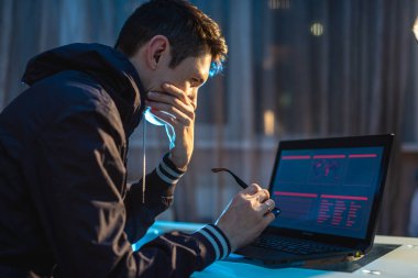 Geceleri dizüstü bilgisayarda gözlüklü bir adam. Freelancer tasarımcı iş yerinde geç kalarak sorunu çözmek için çalışır.