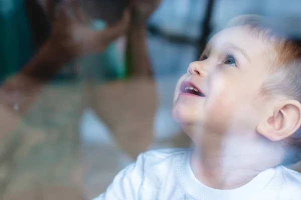 Bébé garçon mignon regardant dans la vitre. Solitude des enfants et attente de la bonté. Orphelinat et orphelins — Photo