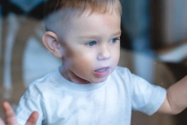 Lindo niño mirando en el cristal de la ventana. La soledad de los niños y la espera de la bondad. Orfanato y huérfanos — Foto de Stock