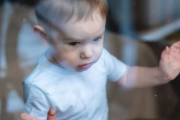 Lindo niño mirando en el cristal de la ventana. La soledad de los niños y la espera de la bondad. Orfanato y huérfanos — Foto de Stock