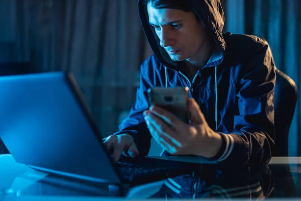 Pria hacker di kap memegang telepon di tangannya mencoba untuk mencuri akses database dengan password. Keamanan Cyber — Stok Foto