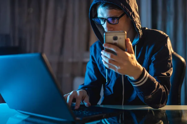 Hacker in the hood holding the phone in his hands trying to steal access databases with passwords. Cybersecurity — Stock Photo, Image