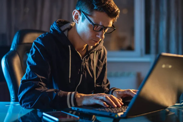 Anak muda dengan kacamata yang bekerja pada laptop di malam hari. Designer atau administrator sistem tetap terlambat bekerja . — Stok Foto