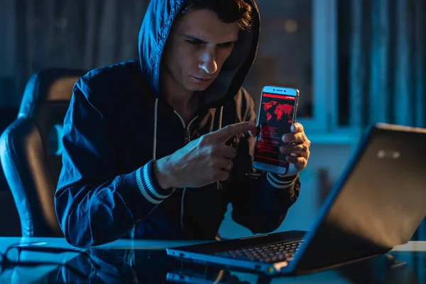Hacker berkerudung memegang telepon di tangannya mencoba untuk mencuri akses database dengan password. Keamanan Cyber — Stok Foto