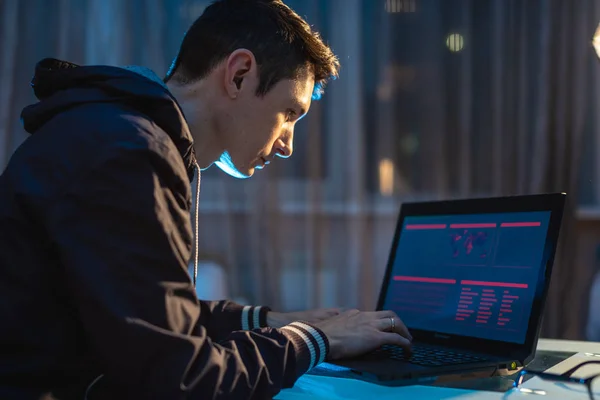 Jeune homme travaillant sur un ordinateur portable la nuit. Designer ou administrateur système sont restés tard au travail . — Photo