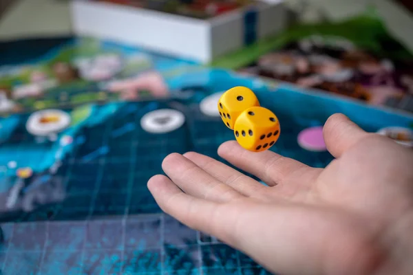 Hand wirft gelbe Würfel auf das Spielfeld. Spielmomente in Dynamik. Konzept der Brettspiele. — Stockfoto