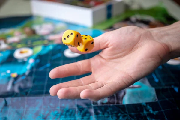 Hand wirft zwei gelbe Würfel auf das Spielfeld. Spielmomente in Dynamik. Glück und Aufregung. Brettspielstrategie — Stockfoto