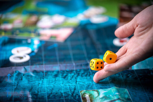 Hand throws two yellow dice on the blue field of the fantasy game. Gaming moments in dynamics. Board games strategy