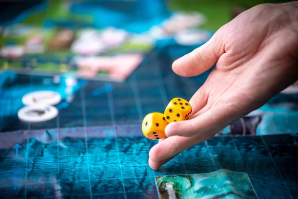 Hand wirft zwei gelbe Würfel auf das Spielfeld. Spielmomente in Dynamik. Glück und Aufregung. Brettspielstrategie — Stockfoto