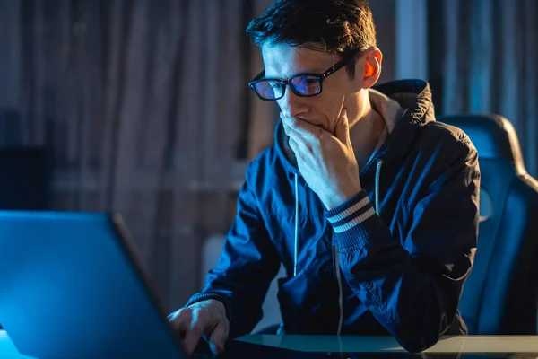 Joven con gafas trabajando en un portátil por la noche. Freelancer está trabajando hasta tarde en un proyecto en casa. — Foto de Stock