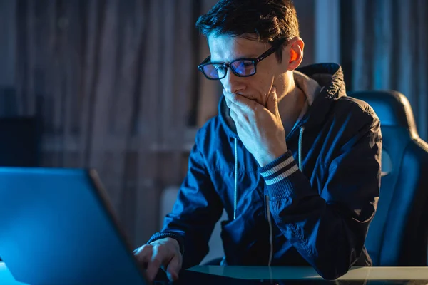 Giovane con gli occhiali che lavora su un portatile di notte. Freelancer sta lavorando fino a tardi su un progetto a casa . — Foto Stock