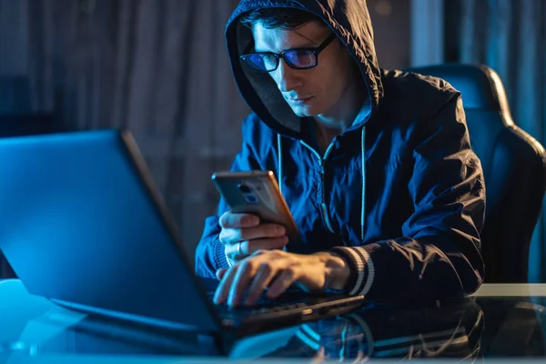 Hacker in the hood holding the phone in his hands trying to steal access databases with passwords. Cybersecurity