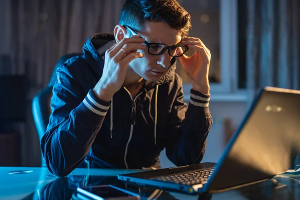 Hombre trabajador con gafas trabajando en un portátil por la noche. Diseñador freelancer o administrador de sistemas se quedó hasta tarde en el trabajo . — Foto de Stock