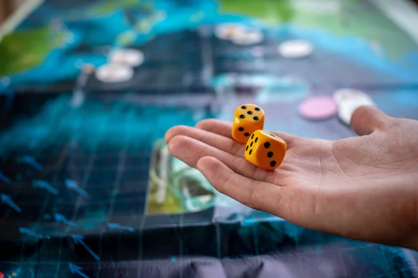 Hand wirft gelbe Würfel auf das Spielfeld. Spielmomente in Dynamik. Konzept der Brettspiele. — Stockfoto