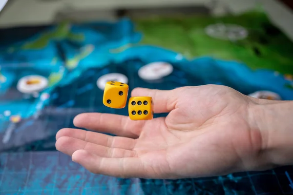 Hand wirft gelbe Würfel auf das Spielfeld. Spielmomente in Dynamik. Konzept der Brettspiele. — Stockfoto