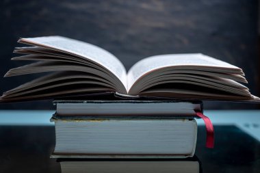 Karanlık bir arka plan üzerinde bir masada kitapların bir yığınına açık kitap. Okullar ve Kolejler sınavlarına hazırlık