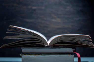 Karanlık bir arka plan üzerinde bir masada kitapların bir yığınına açık kitap. Okullar ve Kolejler sınavlarına hazırlık